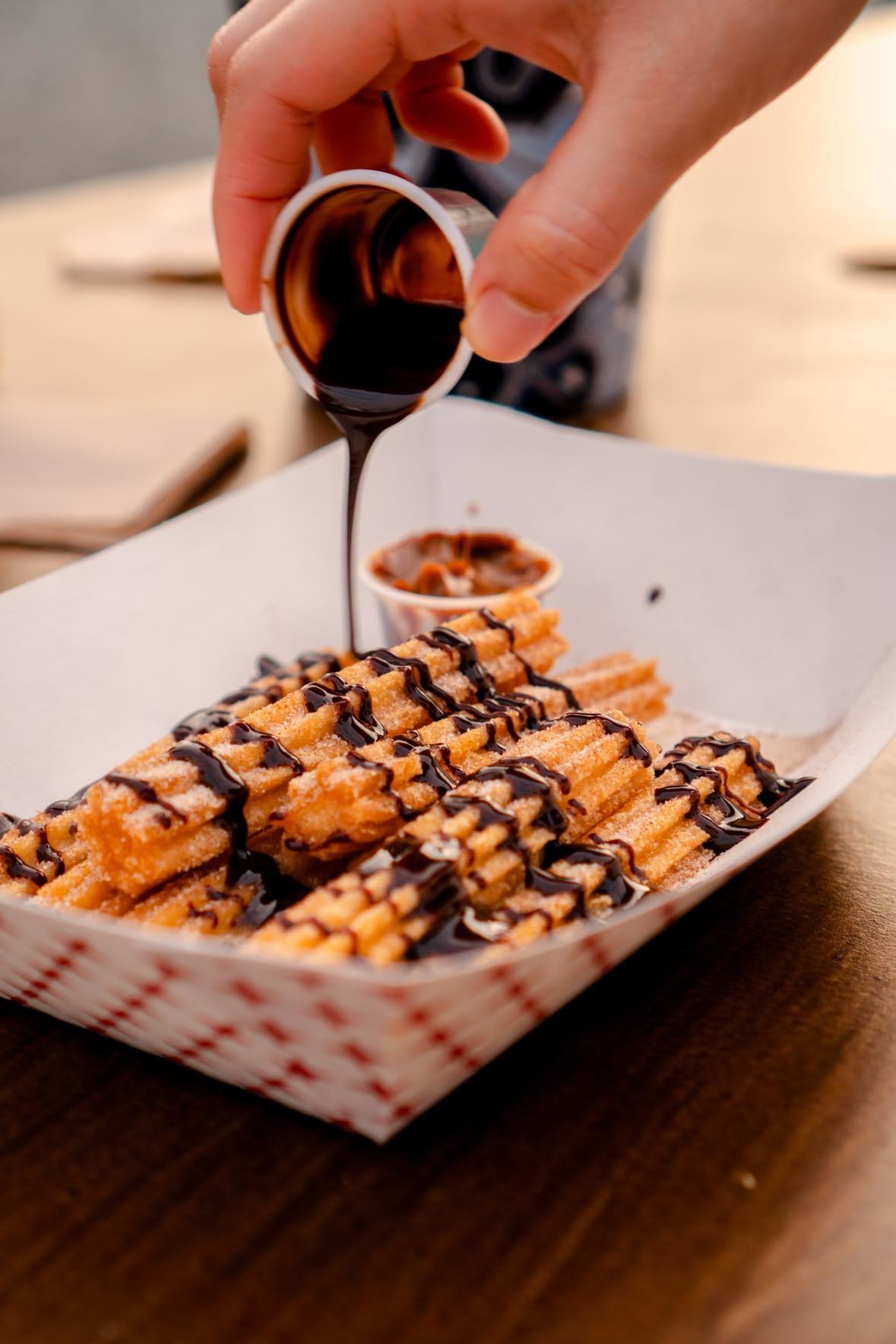 A person drizzling chocolate sauce on a plate of churros.