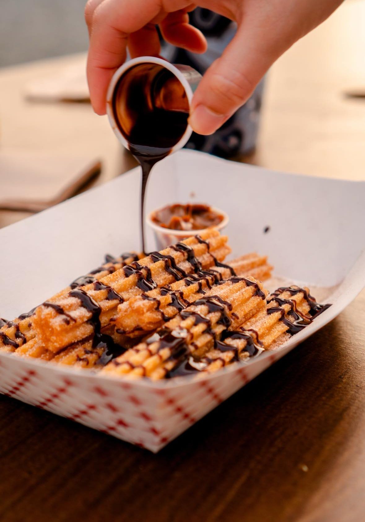 A person drizzling chocolate sauce on a plate of churros.