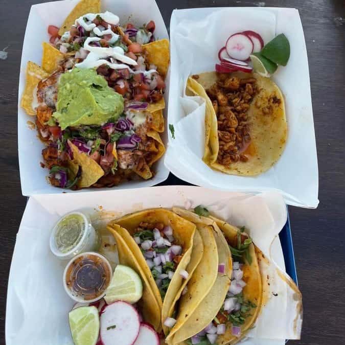 Three tacos with guacamole and sour cream on a wooden table.